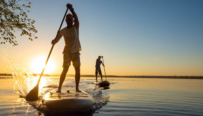 Two people paddleboarding on calm water during sunset