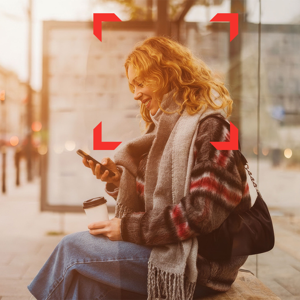 A young woman smiling at her phone as she sits at a bus stop